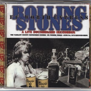 May include: CD case for "Rolling Stones: Ft. Worth Express" live album. The cover features the band's name in blue and white text, with a black and white photo of a concert scene. Includes a bottle of liquor, two Coors cans, and a Coke can.