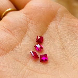 May include: Four square-shaped ruby gemstones in various sizes, displayed on a hand.