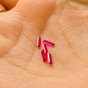 Può includere: Cinque piccole pietre preziose rettangolari rosa su una mano.