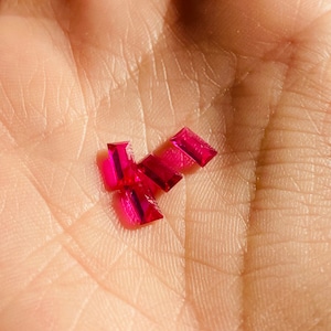 Könnte beinhalten: Eine Gruppe von vier kleinen, rechteckigen, rubinroten Edelsteinen.