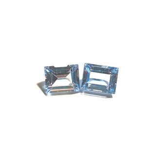May include: Two square-cut, light blue gemstones with a faceted surface. The gems are set against a white background, showcasing their clarity and colour. The gemstones are likely for jewellery making.