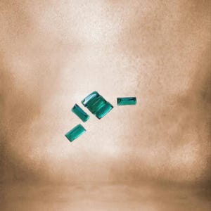 Puede incluir: Un grupo de piedras de cristal rectangulares de color verde azulado dispersas sobre un fondo marrón claro.