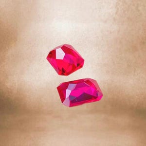 Puede incluir: Dos objetos brillantes de color rojo, facetados, que parecen piedras preciosas, posiblemente de vidrio o plástico, flotan en el aire sobre un fondo marrón claro.