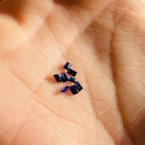 May include: A small pile of dark blue sapphire gemstones, likely for jewelry making.