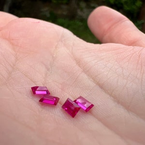 May include: Four pink rectangular gemstones on a hand.