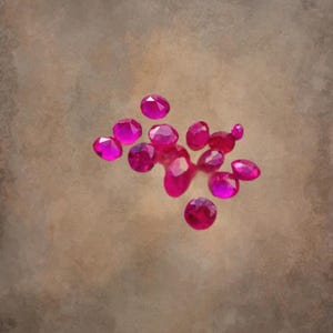 Può includere: Un gruppo di pietre preziose rosa, probabilmente rubini, sparse su una superficie marrone testurizzata. Le pietre preziose sono sfaccettate e hanno una finitura lucida e lucidata.
