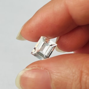 Könnte beinhalten: Ein klarer, rechteckiger, facettierter Edelstein mit einem leichten Blauton.