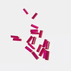 Könnte beinhalten: Eine Streuung kleiner, rechteckiger, rosafarbener Rubin-Edelsteine auf weißem Hintergrund.
