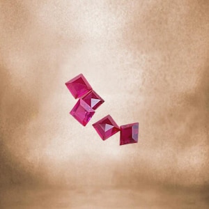 Puede incluir: Cuatro piedras preciosas de color rojo rubí de forma cuadrada sobre un fondo marrón claro.