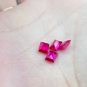 May include: Five pink rectangular gemstones on a white surface.