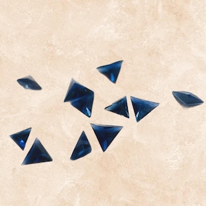 May include: A scattering of dark blue triangular rhinestones on a light beige background.