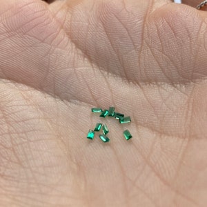 Puede incluir: Una colección de pequeñas piedras preciosas rectangulares verdes en la mano de una persona.