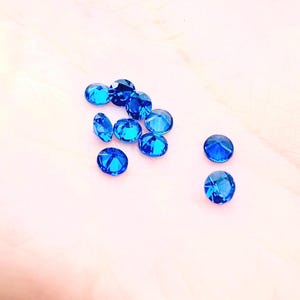 Può includere: Un gruppo di piccole pietre preziose rotonde blu su una superficie rosa chiaro.