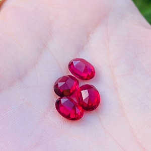 May include: Four oval-shaped, faceted gemstones in a deep red colour. The gemstones are arranged in a cluster on a hand.