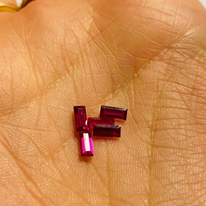 May include: A group of four small, rectangular, ruby red gemstones.
