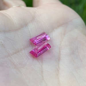 May include: Two pink rectangular gemstones with a faceted cut.