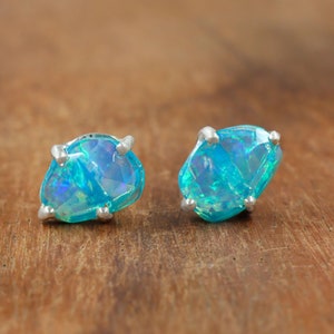 Könnte beinhalten: Ein Paar silberne Ohrstecker mit blauen Opal-Edelsteinen. Die Opale haben eine hellblaue Farbe mit einem Hauch von Grün.