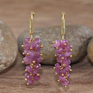 Könnte beinhalten: Ein Paar Ohrhänger mit Anhängern aus rosafarbenen Edelsteinen und goldfarbenen Klappbügelverschlüssen. Die Edelsteine sind facettiert und unregelmäßig geformt, mit kleinen goldfarbenen Perlen. Ein schickes Accessoire.