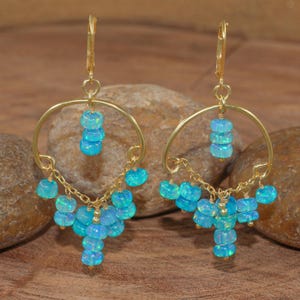 Könnte beinhalten: Ein Paar goldfarbene Creolen mit herabhängenden Clustern aus hellblauen Opalperlen. Die Ohrringe haben einen Klappverschluss und sind vor einem natürlichen Holzhintergrund platziert.
