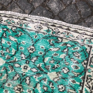 May include: A vintage rug with a teal and white geometric pattern. The rug has a frayed edge and is made of a soft, woven material.