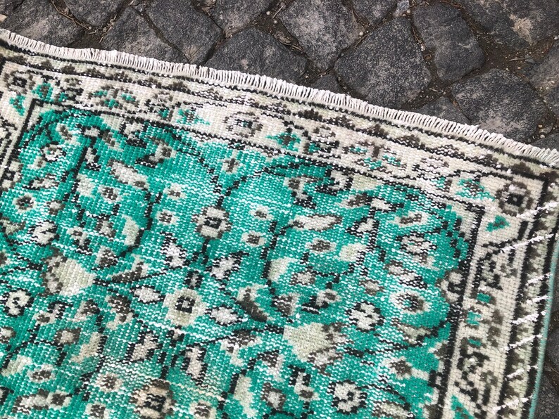 May include: A vintage rug with a teal and white geometric pattern. The rug has a frayed edge and is made of a soft, woven material.