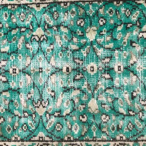 May include: Close-up of a teal and white patterned rug with a floral design. The rug has a distressed look, with some of the colors faded.