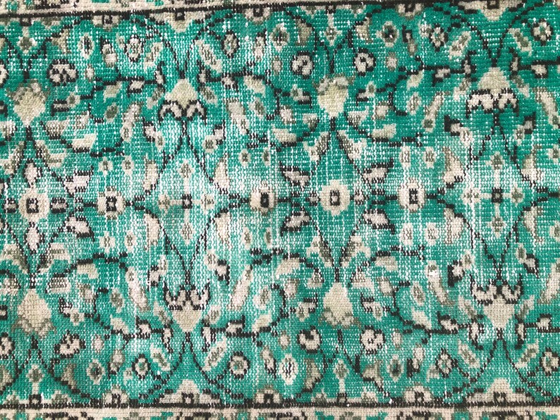 May include: Close-up of a teal and white patterned rug with a floral design. The rug has a distressed look, with some of the colors faded.