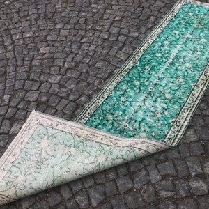May include: A teal and white patterned rug with a floral design. The rug is rolled up and partially unfurled, revealing the underside of the rug.