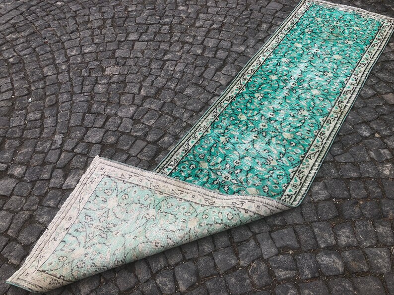 May include: A teal and white patterned rug with a floral design. The rug is rolled up and partially unfurled, revealing the underside of the rug.