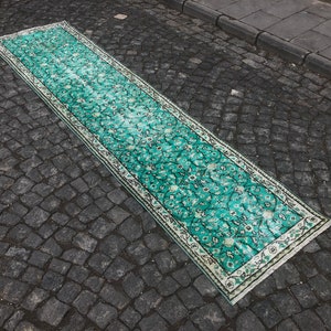 May include: A long, teal-colored rug with a white border and a floral pattern. The rug is laid out on a gray cobblestone surface.