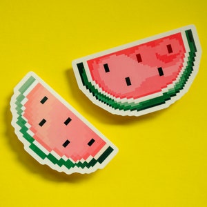 Könnte beinhalten: Zwei pixelartige Wassermelonen-Aufkleber auf gelbem Hintergrund. Die Wassermelonen sind rot mit schwarzen Kernen und grünen Rändern.