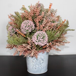 May include: A pink and green floral arrangement in a white metal planter with a crab design. The planter has a distressed finish.