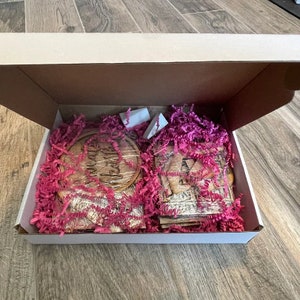 May include: Open box with pink crinkle paper and wooden signs. The signs are round and rectangular with various phrases and words.