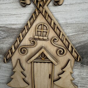 May include: Wooden cutout of a gingerbread house with candy cane accents, a door, windows, and two small trees on either side.