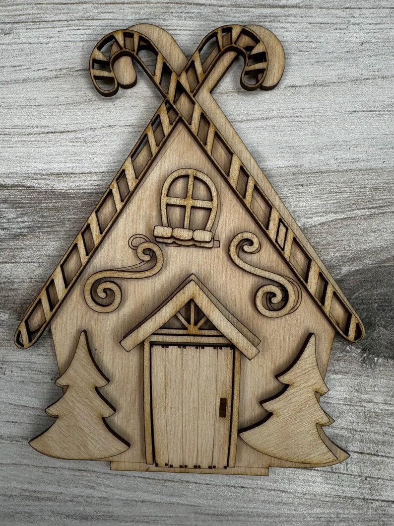 May include: Wooden cutout of a gingerbread house with candy cane accents, a door, windows, and two small trees on either side.