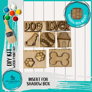 May include: A DIY wood paint kit for a shadow box, featuring wooden cutouts with a dog theme. Includes the words "DOG LOVER", a dog silhouette, paw prints, a baseball, a dog house, and a bone. Also includes paint and a brush.