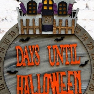 May include: A wooden Halloween countdown clock with a gray background and a black and white haunted house on top. The clock has a black and white number display and the text "DAYS UNTIL HALLOWEEN" in orange letters.