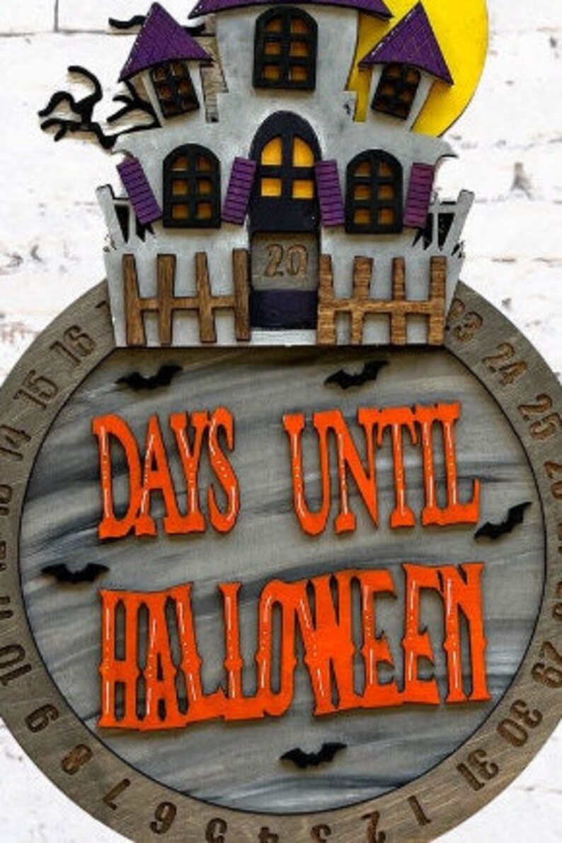 May include: A wooden Halloween countdown clock with a gray background and a black and white haunted house on top. The clock has a black and white number display and the text "DAYS UNTIL HALLOWEEN" in orange letters.