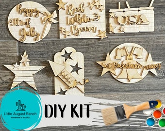 Puede incluir: Un kit de bricolaje con recortes de madera con temas patrióticos. Incluye formas como estrellas, un cohete y letreros con frases como "Happy 4th of July" y "Let Freedom Ring". También se incluye un pincel y botes de pintura.