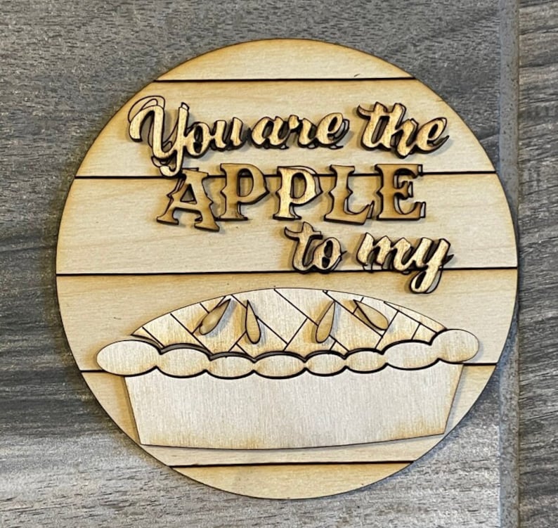 May include: Wooden round sign with the text "You are the APPLE to my" and a cutout of an apple pie.