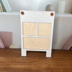 K&ouml;nnte beinhalten: Wei&szlig;es Holzregal mit drei rechteckigen F&auml;chern. Das Regal ist wei&szlig; lackiert und aus Holz gefertigt. Das Regal hat zwei kleine braune Holzrundungen an den oberen Ecken.