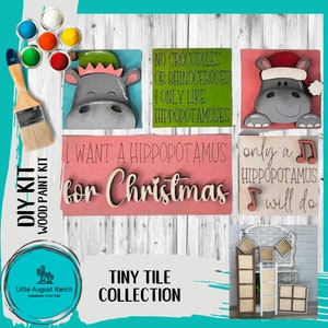 May include: DIY wood paint kit featuring hippopotamus-themed tiny tiles. The kit includes paint, a brush, and several wooden tiles with hippos and phrases like "I want a hippopotamus for Christmas." The collection is handmade in the USA.