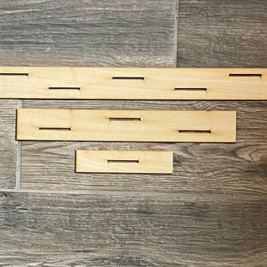 May include: Three wooden strips with cutouts. The top strip has five cutouts, the middle strip has three cutouts, and the bottom strip has one cutout.