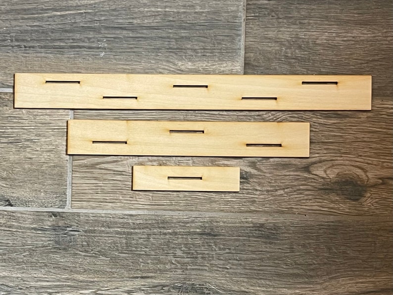 May include: Three wooden strips with cutouts. The top strip has five cutouts, the middle strip has three cutouts, and the bottom strip has one cutout.