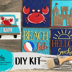 May include: DIY kit for creating a set of five beach-themed wooden signs. The signs feature a blue truck with a crab, a crab, a sandcastle, flip flops, a beach ball, a sun, and the text "Beach", "Beach Please", "Hello Sunshine", and "Life".