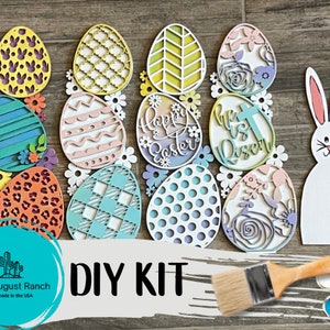 May include: DIY Easter craft kit featuring a bunny, eggs, and flowers. The kit includes a paintbrush and paint pots. The eggs are decorated with various patterns and colors, including pink, blue, yellow, and green. The bunny is white and has a pink nose. The flowers are white and have pink centers. The kit is perfect for creating a festive Easter decoration.