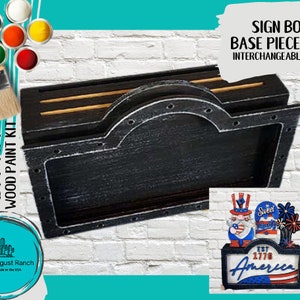 May include: A black wooden sign box base with a distressed finish and a metal frame. The sign box is designed to hold interchangeable signs. The text "SIGN BOX BASE PIECE FOR INTERCHANGEABLE SIGNS" is printed on a white background.