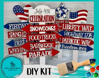 Puede incluir: Kit de bricolaje con letreros de madera con temas patrióticos. Los letreros, pintados en rojo, blanco y azul, muestran flechas que apuntan a "Fuegos artificiales", "Barbecue" y "Desfile". El texto incluye "Celebración del 4 de julio" y "Highway 1776".