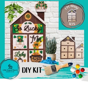 May include: A DIY kit for a wooden house-shaped craft project with a St. Patrick's Day theme. The kit includes a wooden house with six drawers, paint, and a paintbrush. The house is decorated with shamrocks, leprechauns, and the words "We are So Lucky".
