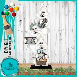 May include: DIY wood paint kit featuring three white bunny rabbits holding Easter eggs and a sign that says "Happy Easter".